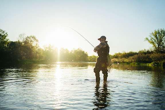 A man fishing in a river at sunset.