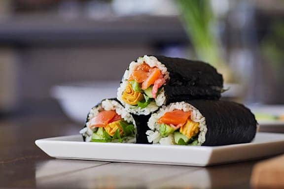 A plate of sushi rolls with vegetables and fish on top.