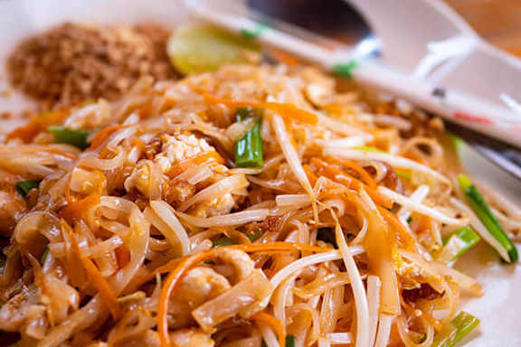 A plate of noodles with a spoon on the side.