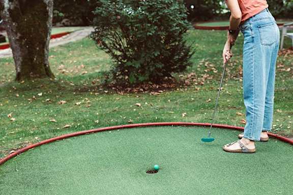 A woman is playing mini golf on a green course.