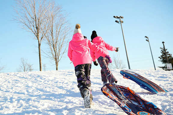 Two people in pink jackets are standing on a snowboard.