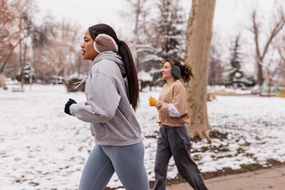 Two women jogging in a snowy park.