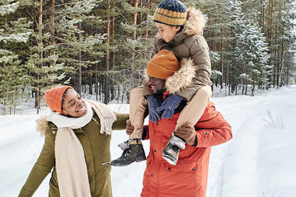 A man is carrying a child on his shoulders in a snowy forest.