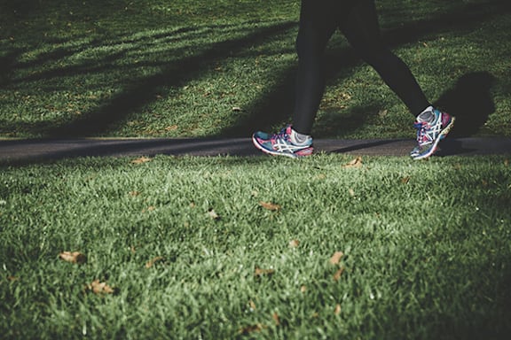 A person is walking on a grassy area with their feet in sneakers.