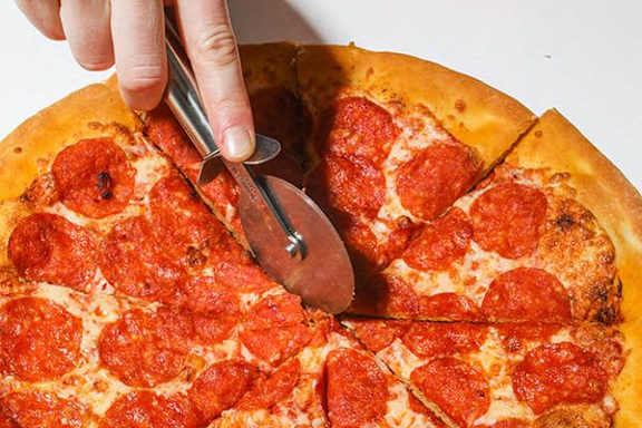 A hand holding a pizza cutter cutting a pepperoni pizza.