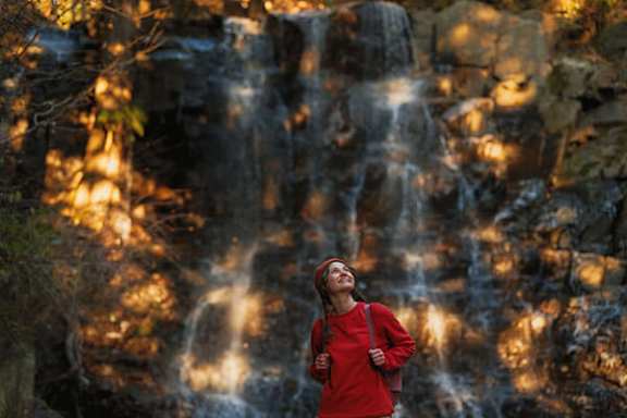 A woman in a red top stands in front of a waterfall.