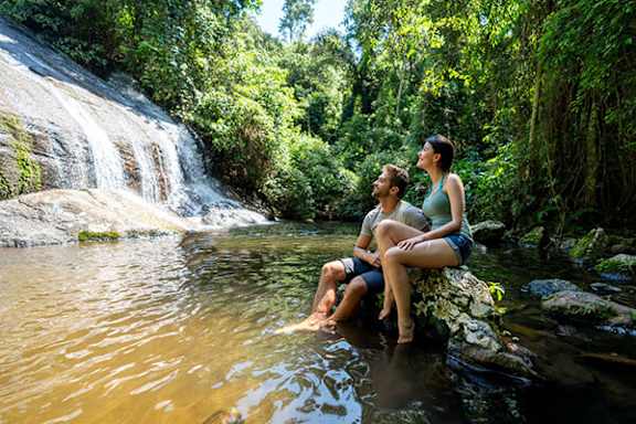 A couple sitting on a rock by a waterfall.