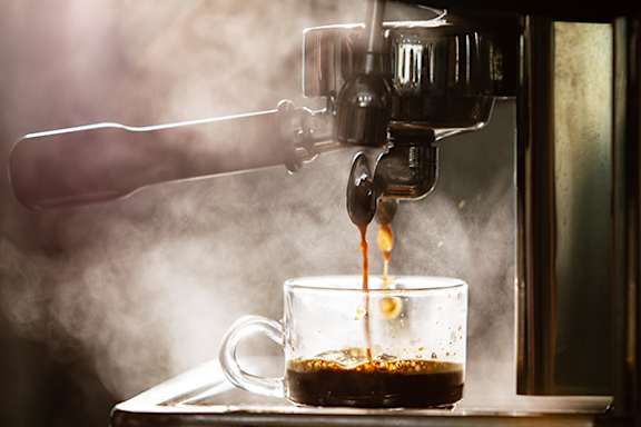 Coffee being poured into a glass cup from a coffee machine.