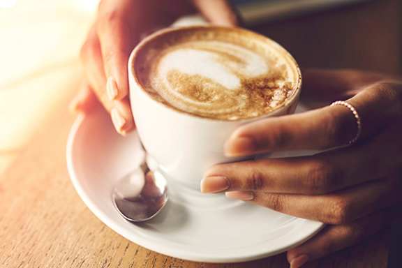 A person is holding a cup of coffee with a spoon in it.