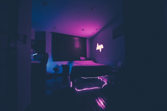 a dark room with a bed and a neon light on the wall