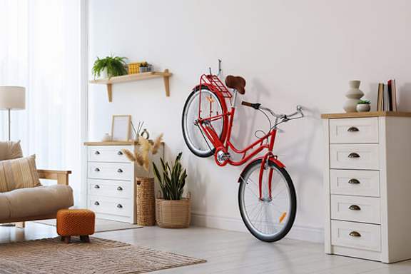 A red bicycle is hanging on a wall in a room with a white dresser and a brown rug.