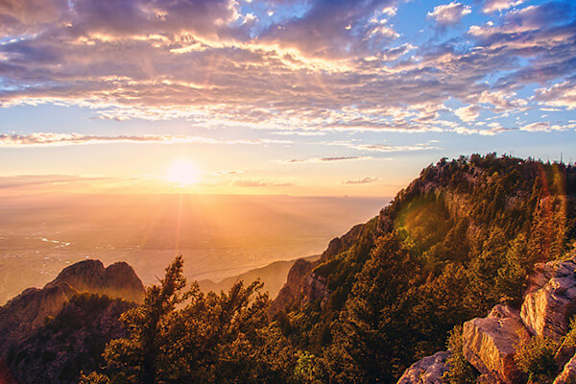 The sun is shining through the clouds over a mountain range.