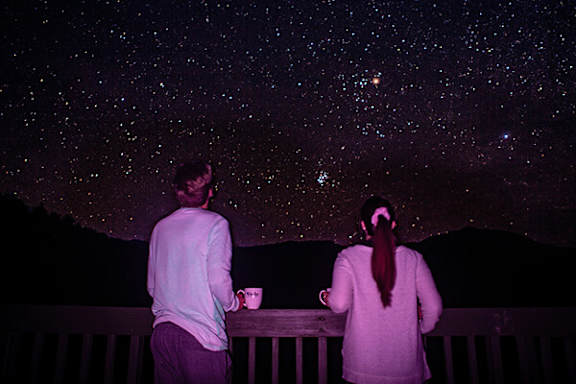 Two people standing on a balcony looking at the stars.