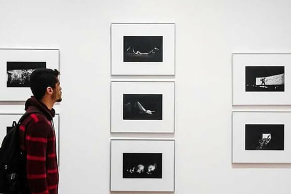a man in a red and black shirt is looking at pictures on a wall