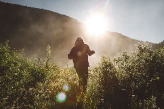 a person standing in a field with the sun behind them