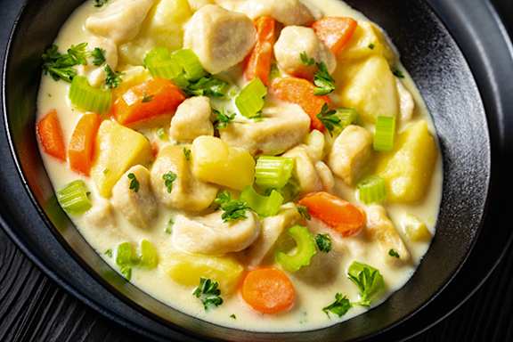 A bowl of creamy chicken stew with carrots, potatoes, and celery.