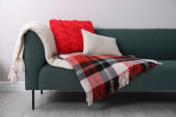 A green couch with a red pillow and a plaid blanket on it.