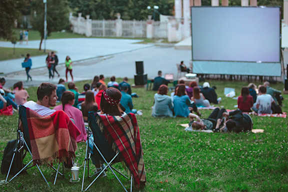 A group of people are sitting on the grass watching a movie in a park.