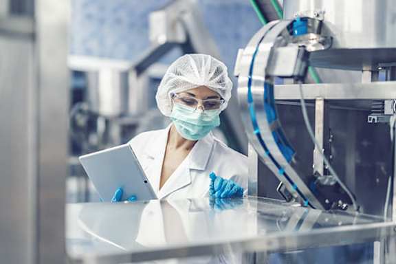 A person in a white lab coat and blue gloves is using a laptop in a laboratory setting.