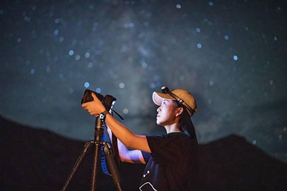 A person in a dark setting is using a telescope.