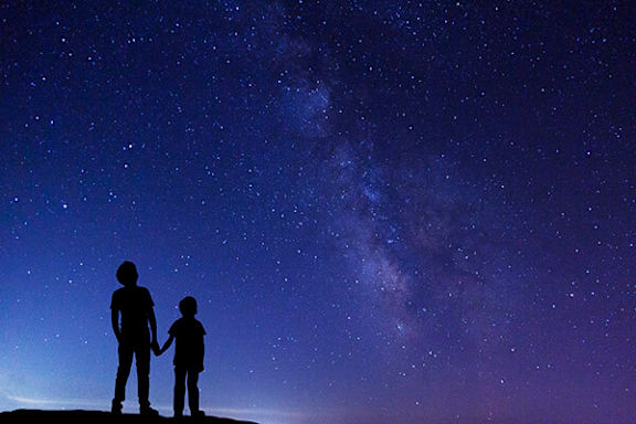 Two people standing on a hill looking at the night sky.
