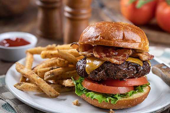 A burger with bacon and cheese is served with fries.