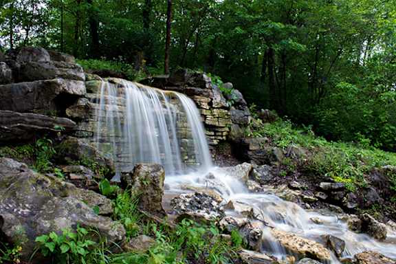 A small waterfall flows over a rocky outcrop in a lush green forest.