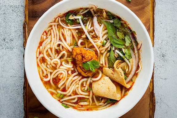 a bowl of noodle soup with tofu and greens on a wooden table