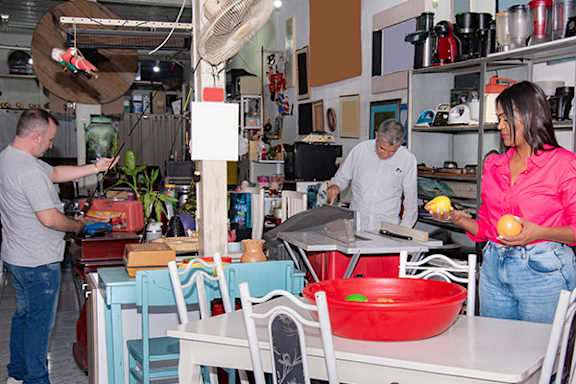 A woman in a pink shirt is holding an apple in a kitchen with two men.