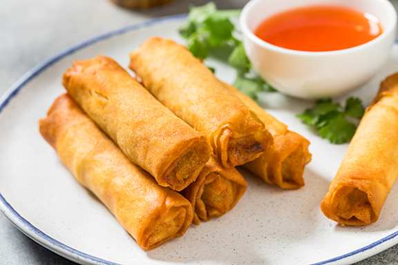 A plate of fried spring rolls with a side of dipping sauce.