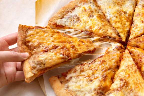 A hand is holding a slice of pizza with melted cheese on it.