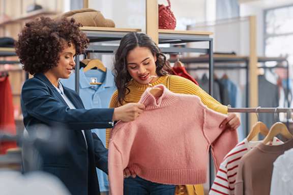 Two women in a clothing store looking at a pink sweater.