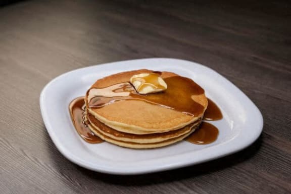 a stack of pancakes on a white plate with syrup