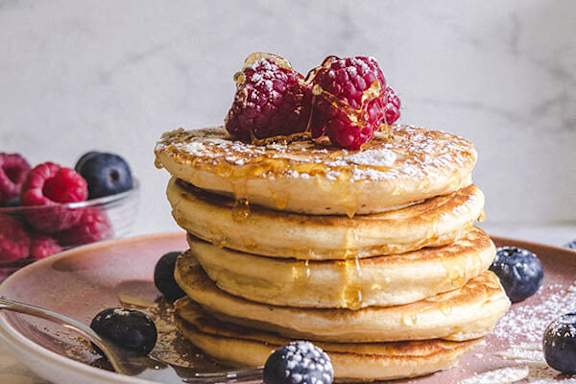 A stack of pancakes topped with raspberries and blueberries.