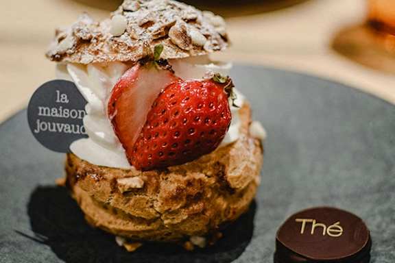 A dessert with a strawberry on top is served on a black plate.