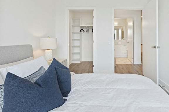 A bed with white sheets and blue pillows is in a room with white walls.