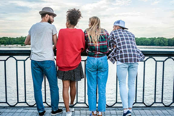 Four people are standing on a bridge looking out over a body of water.