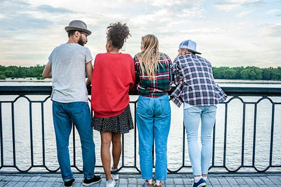 Four people stand on a bridge looking out over a body of water.