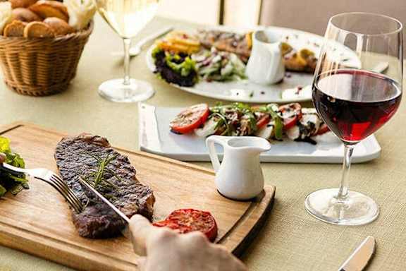 A person is cutting a steak on a wooden cutting board.