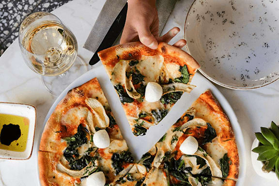 A person is holding a slice of pizza with spinach and mozzarella on a white plate.