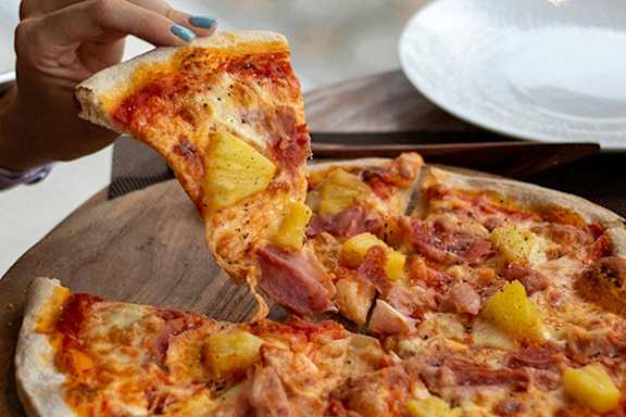 A person is taking a slice of pizza with pineapple and ham toppings.