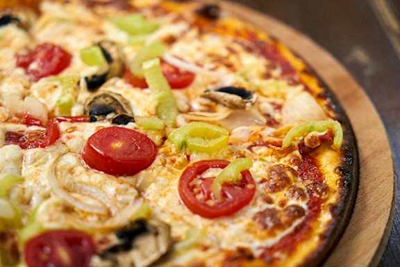 A pizza with tomatoes, onions, and green peppers on a wooden board.