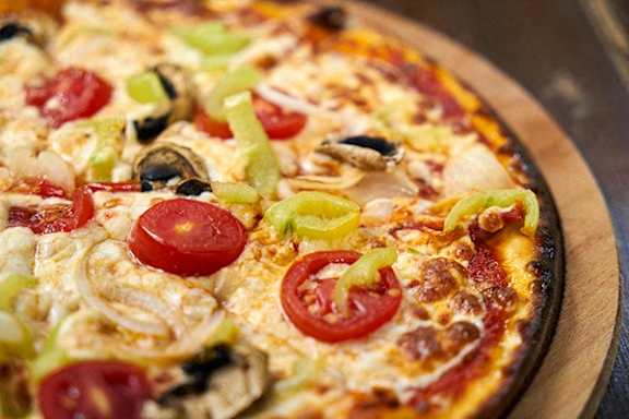 A pizza with tomatoes, onions, and green peppers on a wooden board.