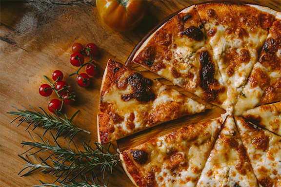 A pizza with tomato and cheese toppings is sliced and served on a wooden board.