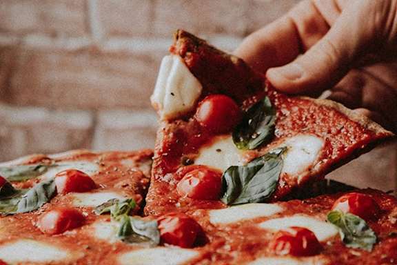 A slice of pizza with tomatoes and basil is being lifted.