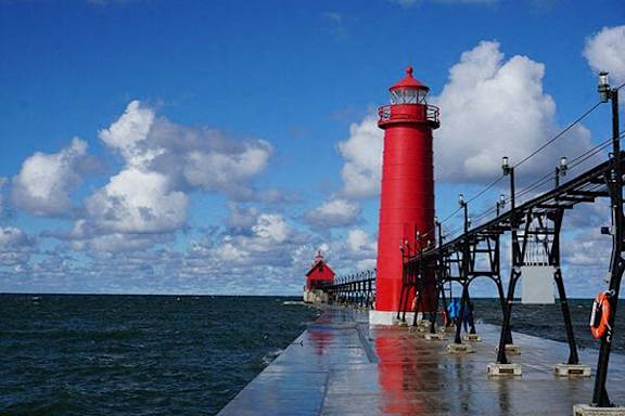 A red lighthouse stands on a pier over the water.