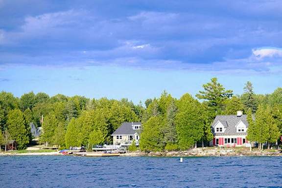 A house with a red roof is situated on a small island in the middle of a lake.