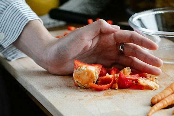 A person is cutting up a red bell pepper on a wooden cutting board.