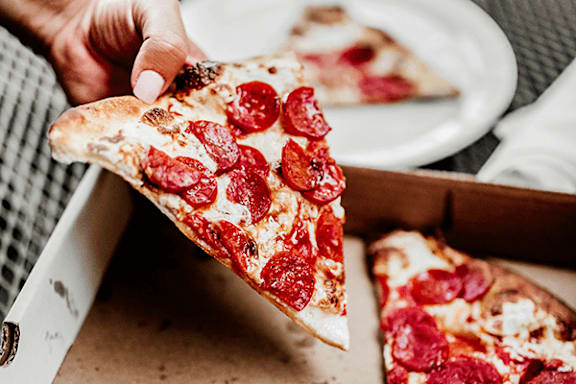 A person is holding a slice of pepperoni pizza.
