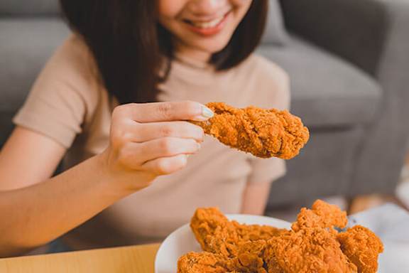 A woman is holding a piece of fried chicken in her hand.